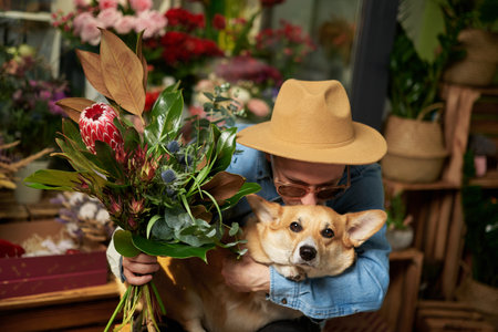 Hipster male person in sunglasses and hat with fresh spring flower bouquet kissing welsh corgi dog. Mothers Day, Valentines Day or International Womens Day concept. High quality imageの写真素材