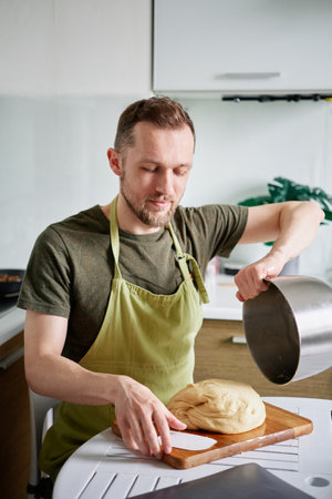 Making pastry at home kitchen concept. Bearded male chef baker in green apron getting out dough from...