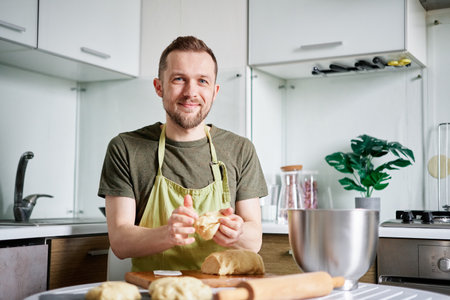 Cheerful caucasian chef baker in green apron making dough balls with wooden cutting board on...