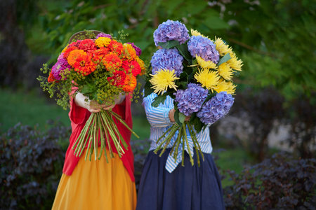 two women holding a bouquet of blue, orange and yellow flowers on the background of green garden , spring summer concept. No faces. High quality photoの写真素材