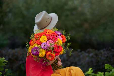 woman holding a bouquet of red, orange and yellow chrysanthemums flowers on the background of green garden , spring summer concept. High quality photoの写真素材