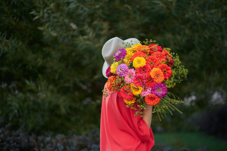 woman holding a bouquet of red, orange and yellow chrysanthemums flowers on the background of green garden , spring summer concept. High quality photoの写真素材