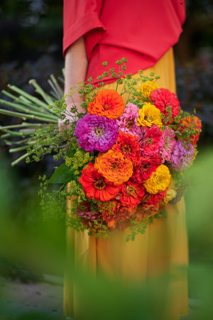 woman holding a bouquet of red, orange and yellow chrysanthemums flowers on the background of green garden , spring summer concept. High quality photoの写真素材