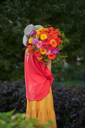 woman holding a bouquet of red, orange and yellow chrysanthemums flowers on the background of green garden , spring summer concept. High quality photoの写真素材