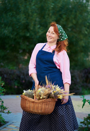 farm woman in apron with basket of dried flowers outdoor, village life. Florist woman with lavender bunches . High quality photoの写真素材