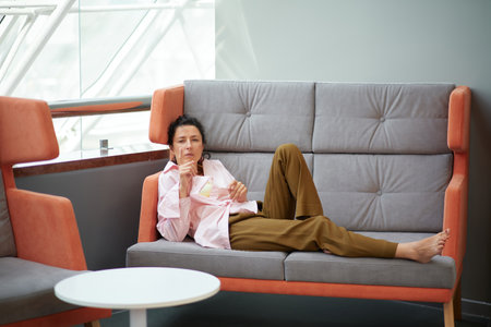 Kick back and relax concept. Young beautiful brunette woman with tired facial expression alone on the couch. Portrait of relaxed female resting at home. High quality photoの写真素材