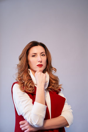 Portrait of a gorgeous caucasian brunette female with wavy hair and brown eyes in elegant burgundy suit with crossed arms, looking at camera, thinking or dreaming. Copy space. High quality photoの写真素材