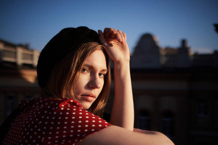 Closeup portrait concept. Cute blonde young caucasian girl in beret and polka dot red dress posing outside in the city looking at camera. Fashion portrait of stylish elegant lady with urban backgroundの写真素材