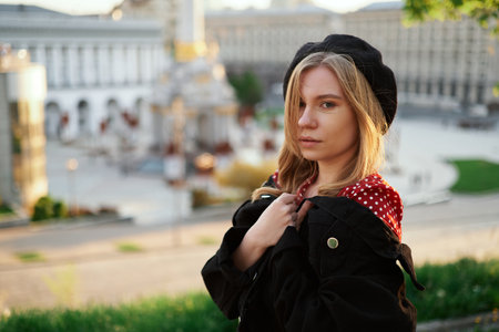 Closeup portrait concept. Cute blonde young caucasian girl in beret, polka dot dress and jacket posing outside in the city looking at camera. Fashion portrait of stylish woman with urban backgroundの写真素材