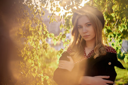 Closeup fashion portrait of adorable stylish blonde young caucasian girl in beret, polka dot dress and jacket posing outside in the city looking at camera with lens flares effect. High quality imageの写真素材