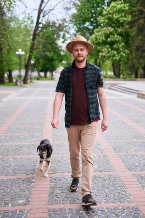 Happy young man in hat walking his rescued dog looking at the camera outdoors. Dog from the shelter found new home High quality photoの写真素材