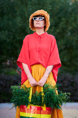 Bright looking female in red t-shirt and yellow skirt with LGBT colors bag full of canabis . High quality photoの写真素材