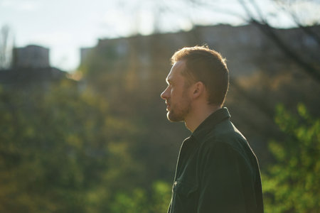 Young man smiling confident standing at park in the sunlight looking aside thoughtfully . High quality photoの写真素材