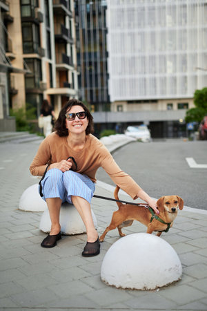 Young female adult in the city with a dog sitting and hugging, smiling. Petting the dog, feeding, having fun High quality photoの写真素材