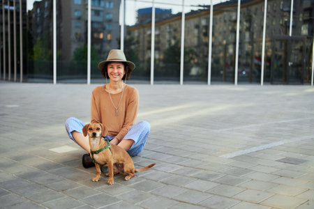 Young female adult in the city with a dog sitting and hugging, smiling. Petting the dog, feeding, having fun High quality photoの写真素材