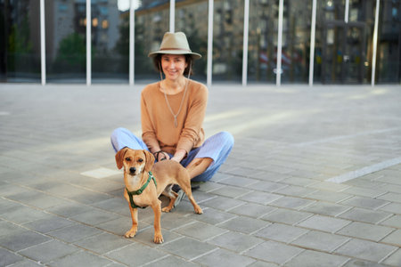 Young female adult in the city with a dog sitting and hugging, smiling. Petting the dog, feeding, having fun High quality photoの写真素材