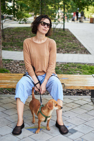 Young female adult in the city with a dog sitting and hugging, smiling. Petting the dog, feeding, having fun High quality photoの写真素材