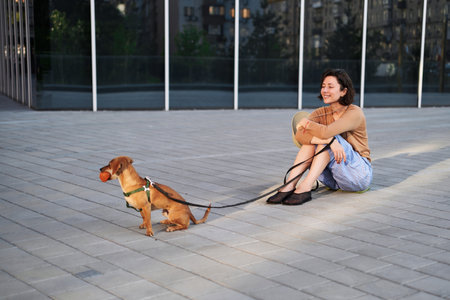 Young female adult in the city with a dog sitting and hugging, smiling. Petting the dog, feeding, having fun High quality photoの写真素材