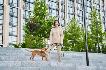 Young pretty female adult with small ginger dog in the bi city walking having fun. City view High quality photoの写真素材