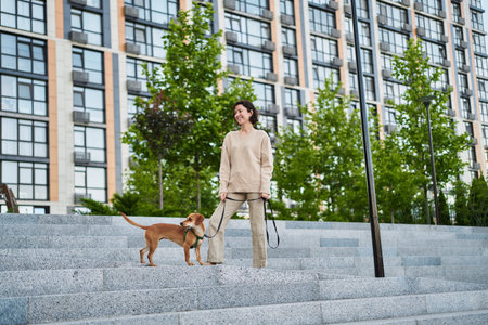 Young pretty female adult with small ginger dog in the bi city walking having fun. City view High quality photoの写真素材
