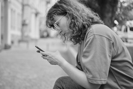 gorgeous beautiful young woman with red hair messaging on the smart-phone at the city street background. pretty girl having smart phone conversation in sun flare. . High quality photoの写真素材