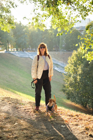 Caucasian girl dachshund owner walking with dog in park outdoors, autumn vacation. Domestic pet concept. Friendship between human and pet. Funny puppy wearing sweater. High quality vertical photoの写真素材