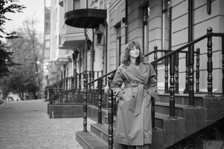 Young, attractive, successful business woman, confidently looking forward on the background of old city scape. Evening sun, brown hair and trench coat. Confidence concept. High quality photoの写真素材