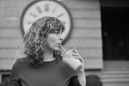 Watch the time concept. woman in dark red dress with cold tea next to huge watch over her head . Young brunette woman is looking at clock. Keep track of time. High quality photoの写真素材