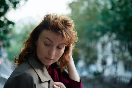 Cropped closeup portrait of a caucasian mature beautiful woman wife looking at the sun in park outdoors streets hiding from the sunset sun in sad serious mood. High quality photoの写真素材