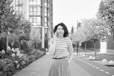 Happy young woman walking outside. One confident girl walks outdoors in street smiling. Urban city, residential complex, real estate concept. Brunette female adult in pink clothes. High quality photoの写真素材