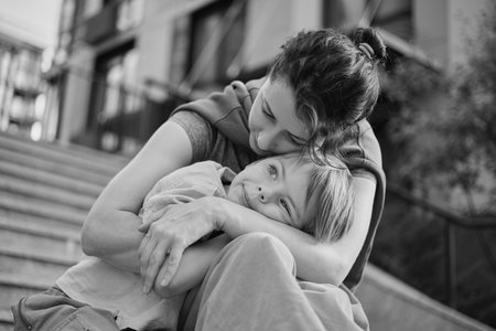 Happy family: mother and child son hugging and laugh sitting on the city stairs. motherhood concept, togetherness, love emotion. Urban city concept, residential complex in Ukraine. High quality photoの写真素材