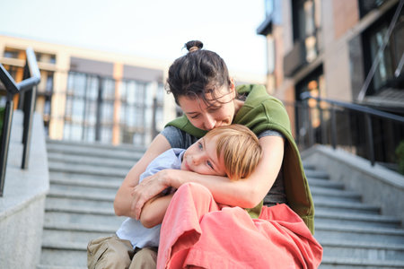 Happy family: mother and child son hugging and laugh sitting on the city stairs. motherhood concept,...