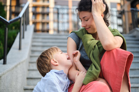 Happy family: mother and child son hugging and laugh sitting on the city stairs. motherhood concept, togetherness, love emotion. Urban city concept, residential complex in Ukraine. High quality photoの写真素材