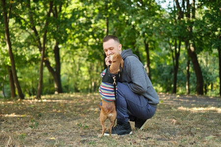 man with his cute puppy in a sweater in the park training, feeding, smiling. Spring, summer, autumn handsome man having fun with his dog outdoor. Space for text. High quality photoの写真素材