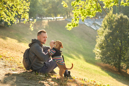 man with his cute puppy in a sweater in the park training, feeding, smiling. Spring, summer, autumn...