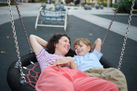 Happy Young mother playing with her son on the playground, hugging, laughing. having fun together on the weekend sunny day. School playground. High quality photoの写真素材