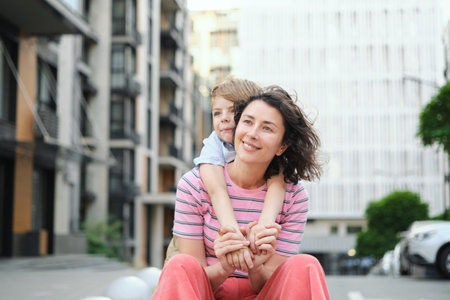 young mother and son smiling looking at the camera in modern residential complex. Having fun together, happy parenting, new home concept. Bright summer day in the urban background. High quality photoの写真素材
