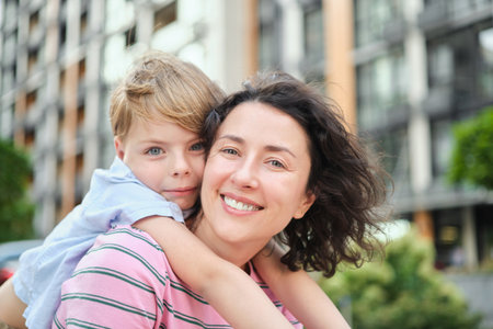 young mother and son smiling looking at the camera in modern residential complex. Having fun together, happy parenting, new home concept. Bright summer day in the urban background. High quality photoの写真素材