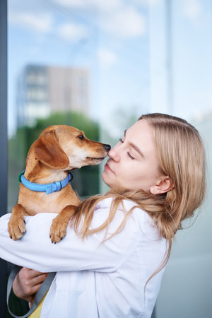 Young veterinarian smiling and holding dog near the vet clinic entrance. Healthy dog, diagnostic, treatment of domestic animals. High quality photoの写真素材
