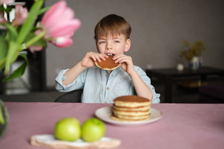 Little boy adorable having breakfast with pancakes with tea and apples at home. Cute weekend with sweet tasty food and emotional child. High quality photoの写真素材