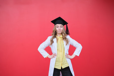 Young blond female in medical uniform and graduation cap looking at the camera and smiling. Standing outside, happy to finish studying in healthcare or veterinary. High quality photoの写真素材