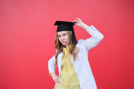 Young blond female in medical uniform and graduation cap looking at the camera and smiling. Standing outside, happy to finish studying in healthcare or veterinary. High quality photoの写真素材