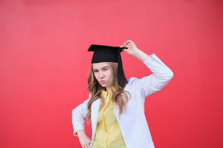 Young blond female in medical uniform and graduation cap looking at the camera and smiling. Standing outside, happy to finish studying in healthcare or veterinary. High quality photoの写真素材