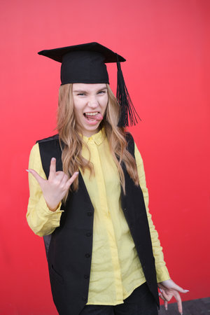 Young beautiful blond female in graduation cap with emotional facial expression on red background. Happy to finish school, college or university High quality photoの写真素材