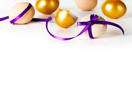 Easter egg with violet bow on white background. Composition with beige and gold eggsの写真素材