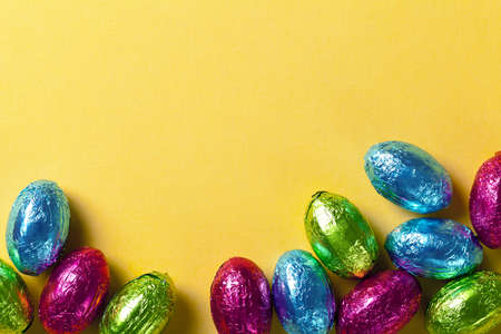 Easter background with colorful chocolate eggs on yellow paper  Top view, macro shot
