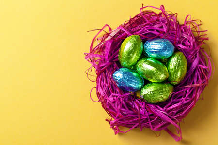Easter eggs in pink nest  Holiday composition on yellow paper background  Top view  Macro shot