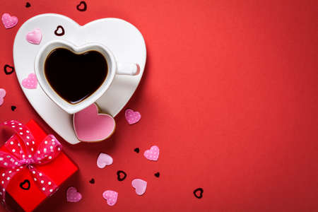 Coffee with red gift box and cookie in shape of heart. Composition for Valentines Day on red paper background. Top view. Copy spaceの写真素材