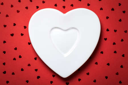 Heart form white plate on red paper background. Top view の写真素材