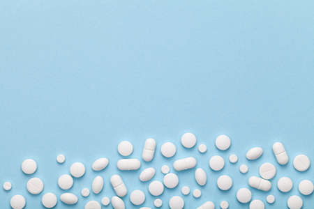 White medical pills on blue background. Copy space. Top view